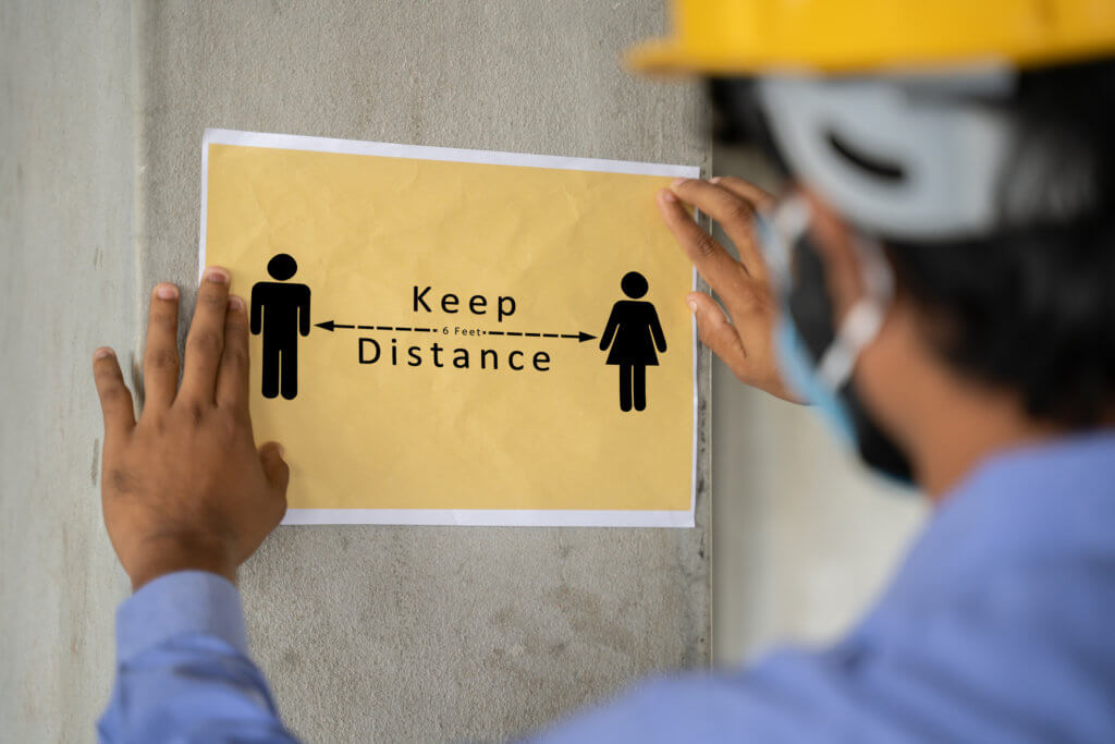 worker pasting Keep 6 feet distance on wall at work place or construction site due to coronavirus or covid-19 pandemic - concept of safety measures, back to work, new normal and protection.