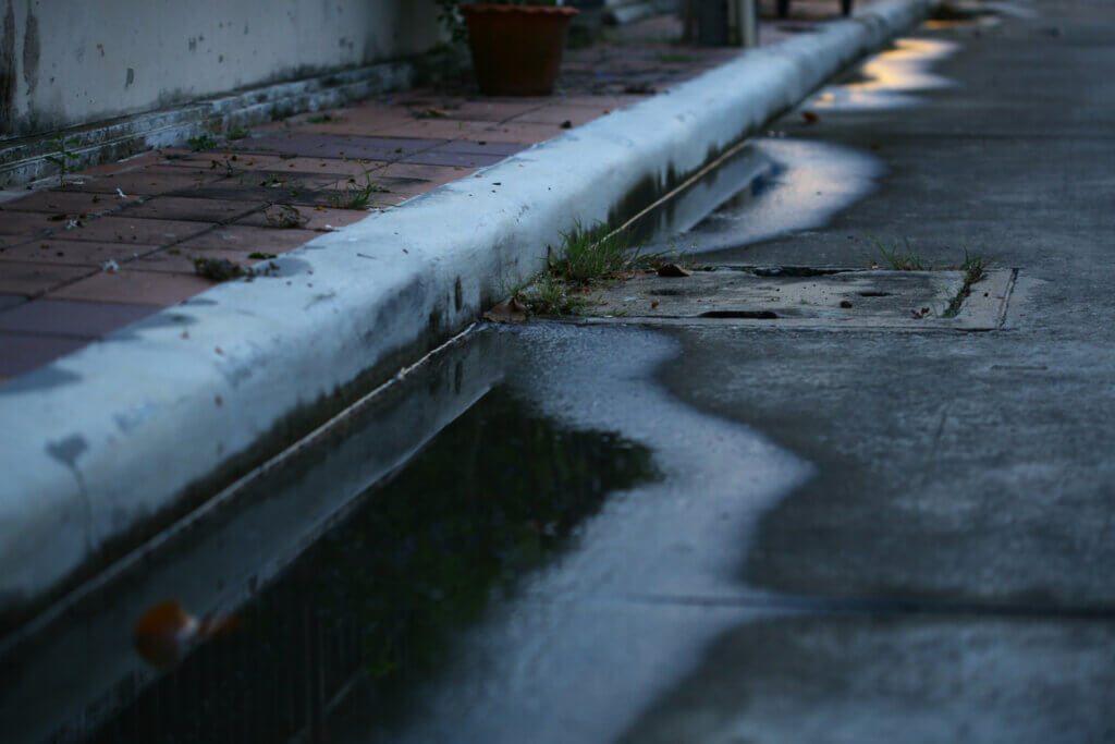 Catch basin with poor drainage system left water near catch basin drain inlet on a concrete road.